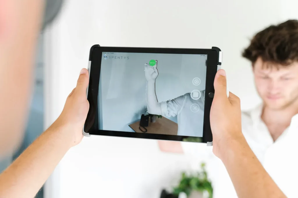 Person holding a tablet that displays a 3D scan of an arm with a measurement overlay, illustrating ARKit LiDAR point clouds used for sizing