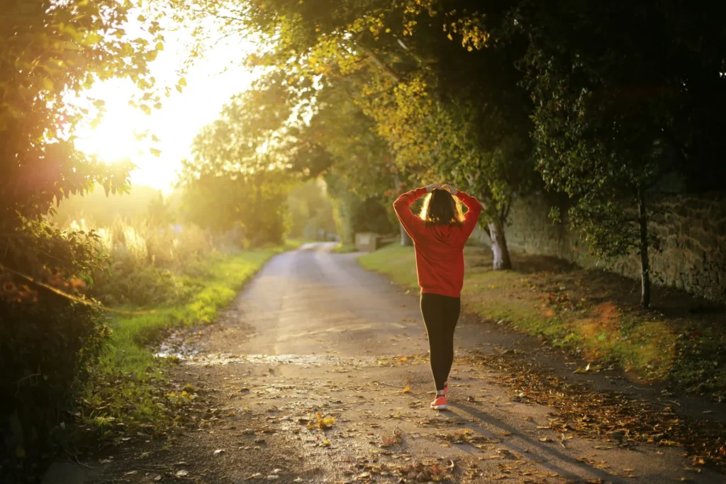 Woman in a red hoodie walking along a sunlit tree-lined path at sunset, evoking calm and well-being for HIPAA-compliant mental health app agencies