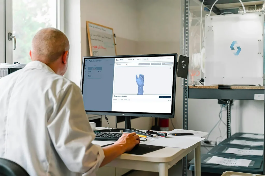 Technician in a lab coat reviewing a 3D scan of a patient's arm on a computer screen next to a 3D printer, illustrating Canadian 3D scanning app agencies